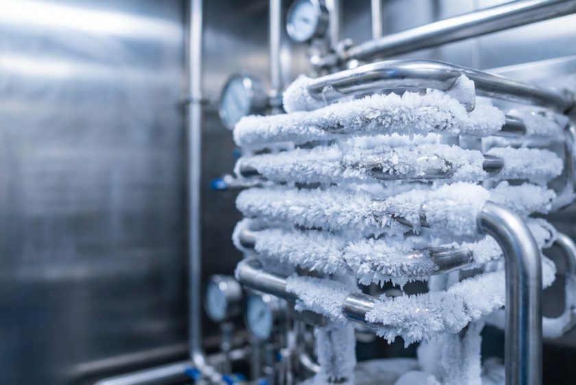 Bir liyofilizatörün kondenser ünitesindeki paslanmaz çelik serpantinlerin üzerinde yoğun bir şekilde birikmiş beyaz, kristalize buzun yakın çekim fotorealistik görüntüsü.